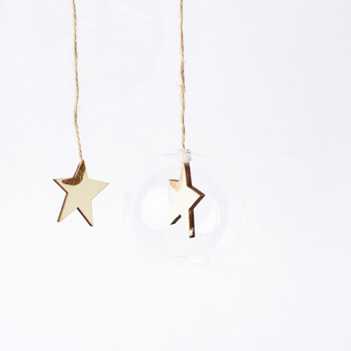 A clear glass ornament with a gold star inside, hanging by a twine string.