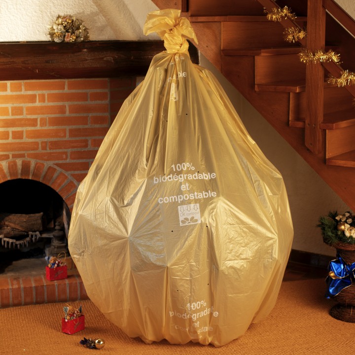 A large, shiny gold trash bag shaped like a festive present near a cozy fireplace.