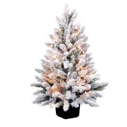 Sneeuwbedekte kunstkerstboom met zachte verlichting in een zwarte pot.