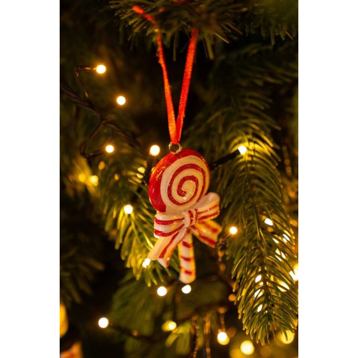 A festive ornament resembling a candy swirl hangs on a green tree, glowing softly with lights.