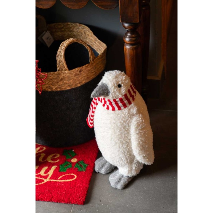 A fluffy white penguin figurine wearing a red-striped scarf stands near a woven basket.