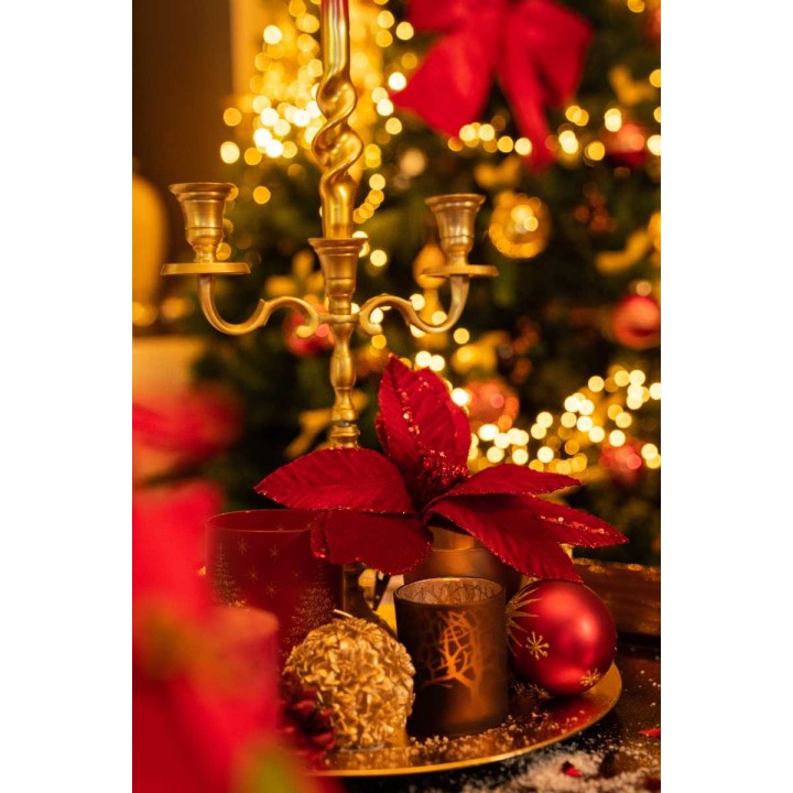 A festive table with a golden candlestick, red poinsettias, and sparkling holiday decor.