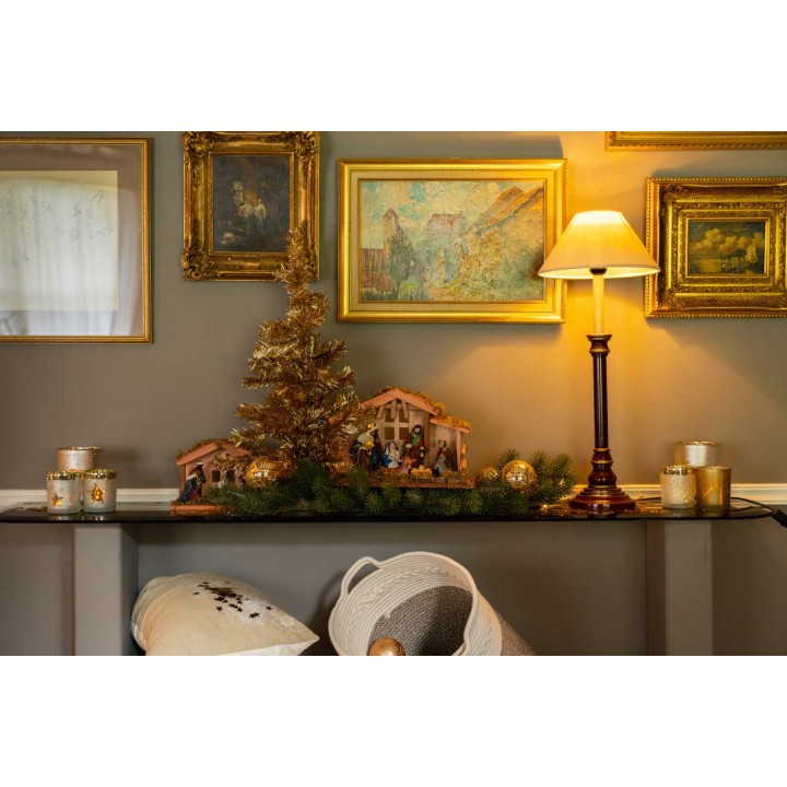 Décor festif avec un sapin doré, crèches, tableaux dorés et lumière chaleureuse.
