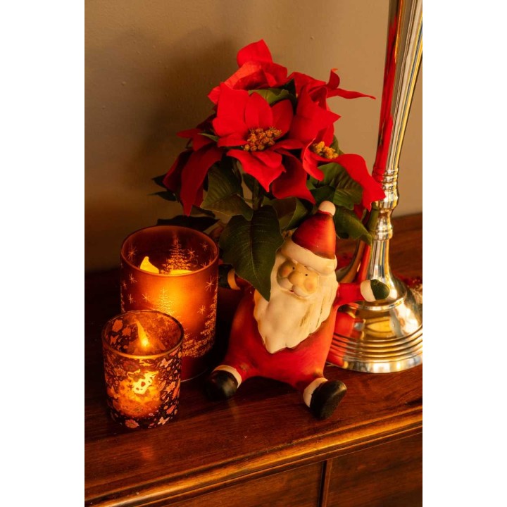 Poinsettias rouges, bougies lumineuses et un Père Noël en tissu sur une table en bois.