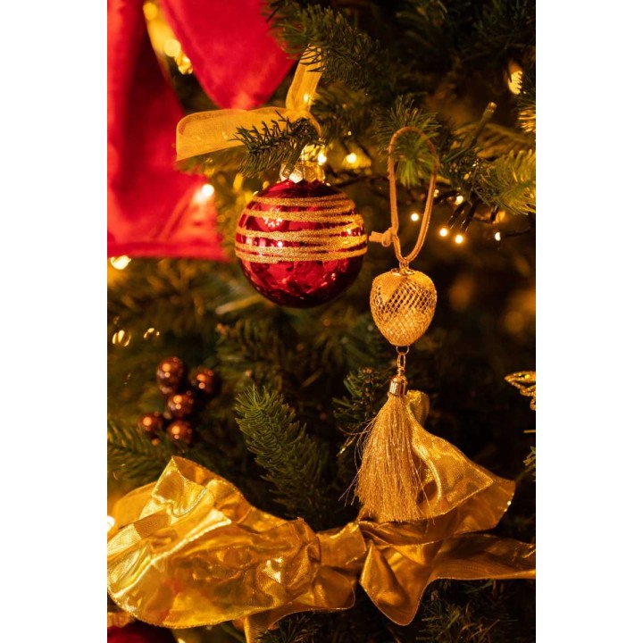 Gouden en rode kerstversieringen hangen aan een groene dennenboom, omgeven door warme lichtjes.