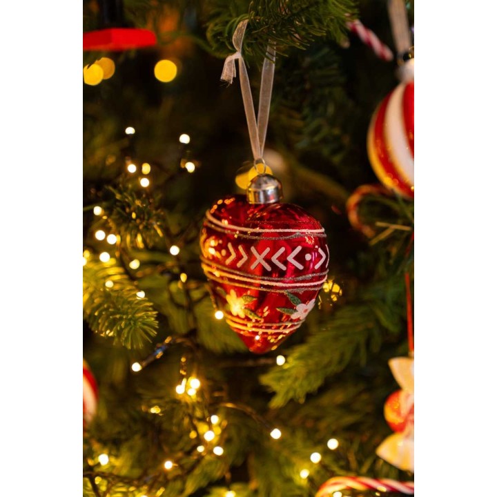 A shiny red ornament with white patterns hangs amid twinkling lights on a festive tree.