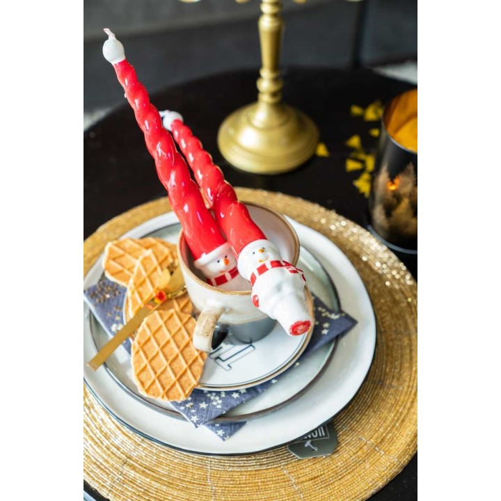 A festive table setting with red twisted candles, a snowman mug, and golden accents.