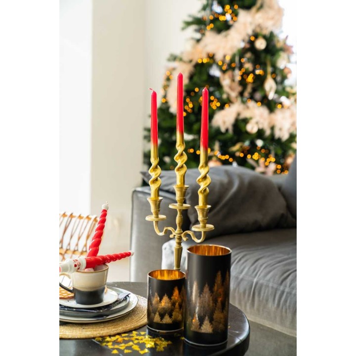 Bougeoir doré avec bougies rouges, décor festif et arbre illuminé en arrière-plan.