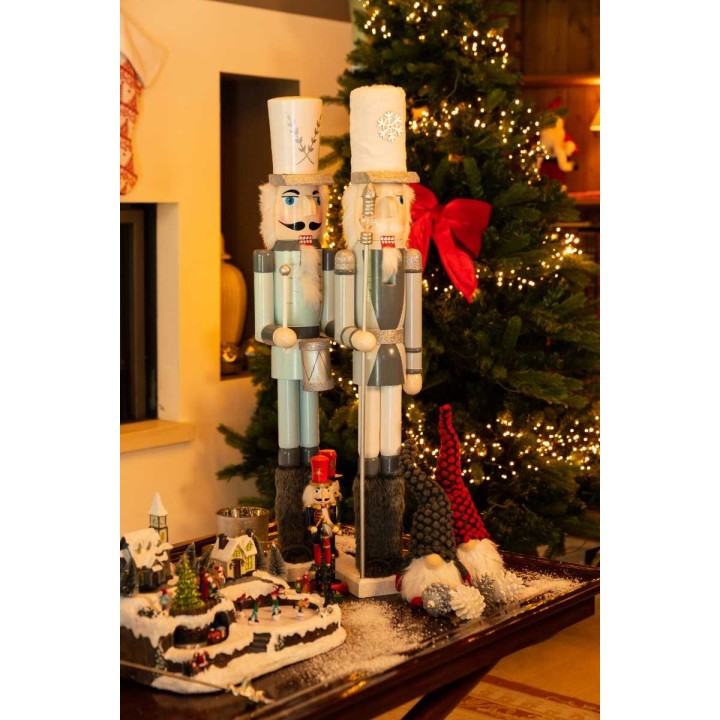 Two large nutcracker figures stand beside a decorated Christmas tree and festive tabletop display.