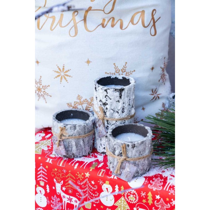 Three rustic candle holders made from bark, placed on a festive red tablecloth with seasonal prints.