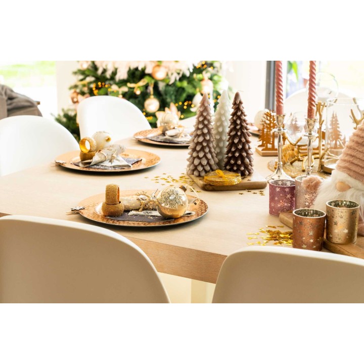 Table élégamment dressée avec décorations dorées et sapin en arrière-plan.