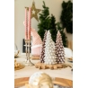 Pastel-colored candles shaped like trees, surrounded by festive decor and soft greenery.