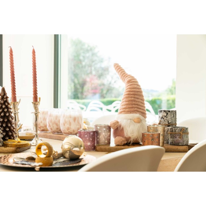 A cozy holiday table with candles, decorative gnome, and textured ornaments.