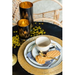 Een elegante tafelsetting met een gouden placemat, een witte kop, koekjes en sfeervolle kaarsen.