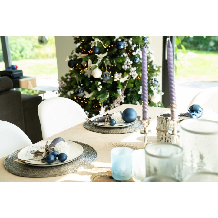 A festive dining table with elegant blue accents, surrounded by a decorated Christmas tree.