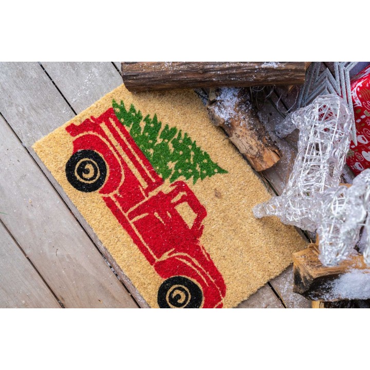 A cozy doormat featuring a red vintage truck carrying a green Christmas tree on a beige background.