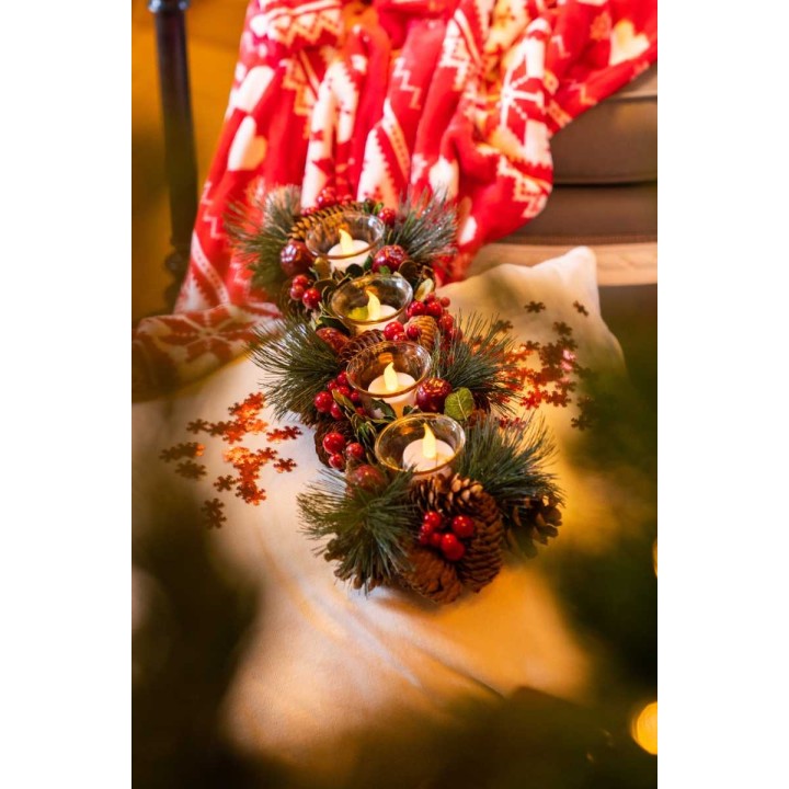 A cozy winter scene with candles surrounded by pine branches and festive decorations.