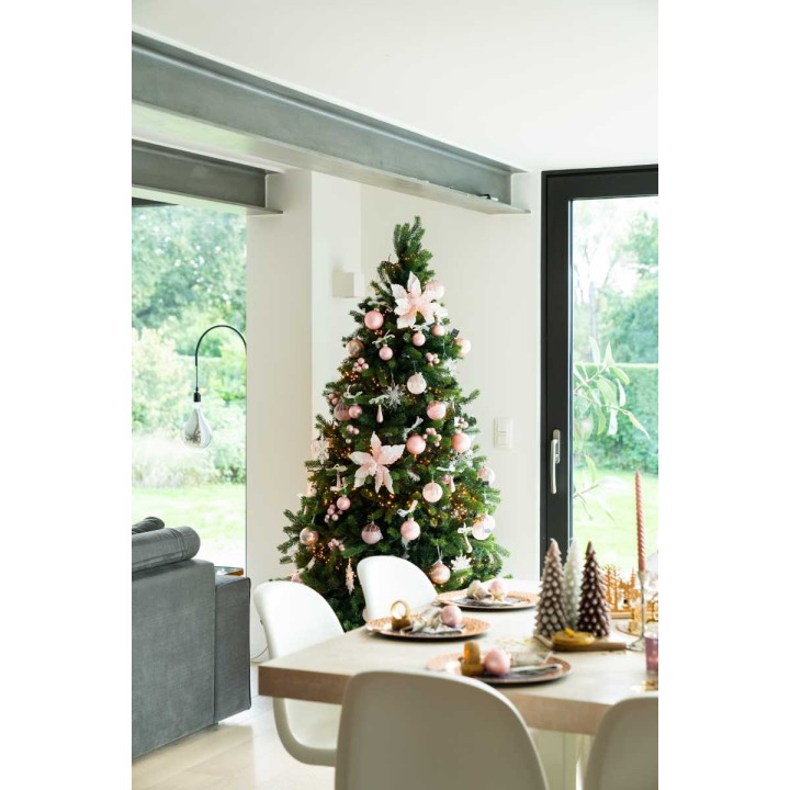 A beautifully decorated Christmas tree with pink ornaments and flowers, next to a cozy dining area.