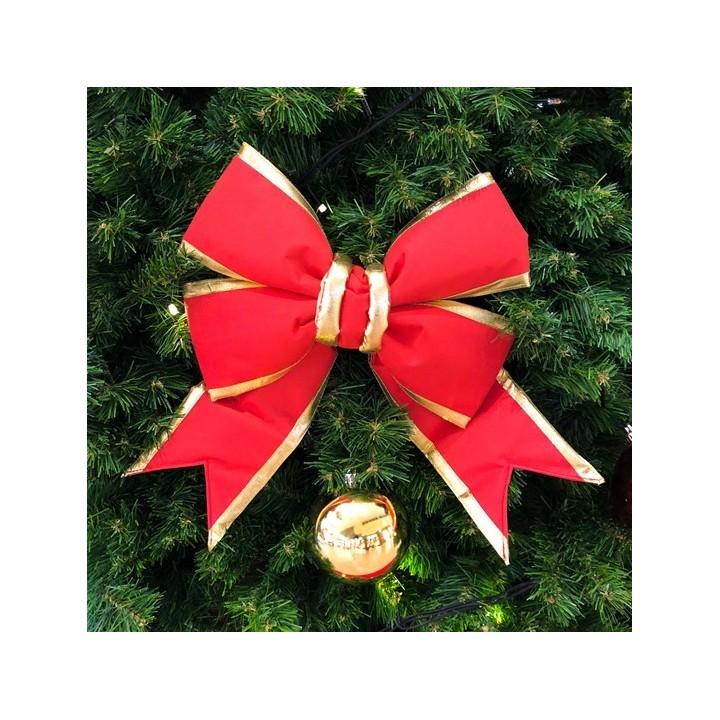 Een grote, rode strik met gouden rand versiert een groene kerstboom, omringd door decoraties.
