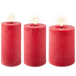 Drie rode kaarsen met een warme vlam, van verschillende hoogtes, op een lichte achtergrond.