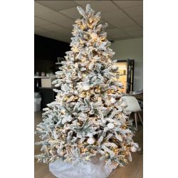 A frosted Christmas tree adorned with warm lights and white ornaments, set in a cozy room.