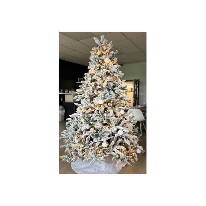 Sapin enneigé décoré de lumières dorées et de boules blanches, ambiance festive chaleureuse.
