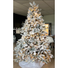 A frosted Christmas tree adorned with warm lights and white ornaments, set in a cozy room.