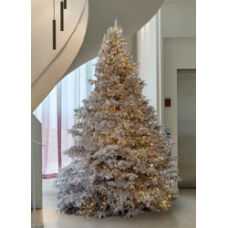 Un sapin blanc lumineux décoré, illuminé par des guirlandes dorées, dans un intérieur moderne.