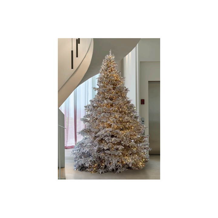 Un sapin blanc lumineux décoré, illuminé par des guirlandes dorées, dans un intérieur moderne.