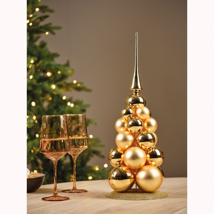A festive gold ornament tree beside elegant champagne glasses, glowing softly in warm light.