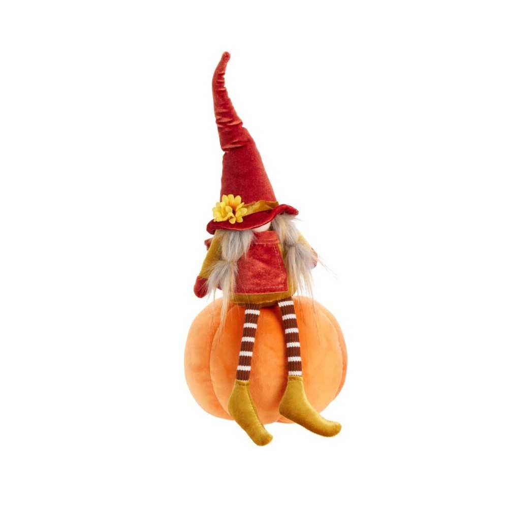 Een schattige pop met een rode hoed zit op een oranje pompoen, met gestreepte sokken.
