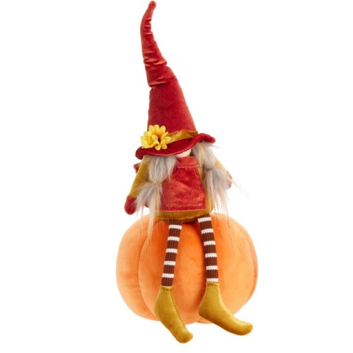 A whimsical doll in a red hat sits on a plush orange pumpkin, with striped stockings.