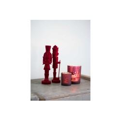 Figurines rouges en bois et bougie décorative sur une surface claire et texturée.